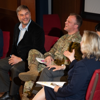 A group of five panelists sit on stage, laughing and smiling. 