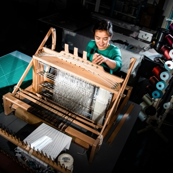 The photograph shows a researcher working with a loom that generates fibers in the advanced fibers/fabrics lab
