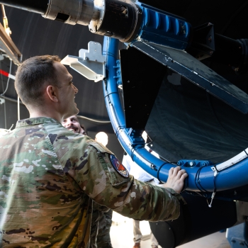 A uniformed member of the U.S. Air Force looks into a large telescope setup.