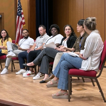A group of seven staff members sit on chairs on a stage while sharing in a panel discussion.