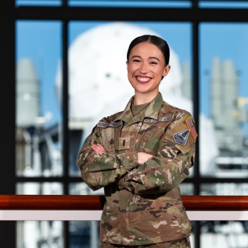 Military fellow Kelsey Monaghan-Bergson smiles for a photo in the Lincoln Laboratory lobby, with radar antennas visible outside in the background.