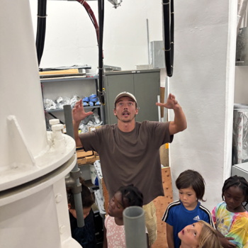 During a tour of a Ground-Based Radar dome, a Laboratory staff member animatedly explains to 5 young school children how the radar is re-positioned to point at different objects of interest.  