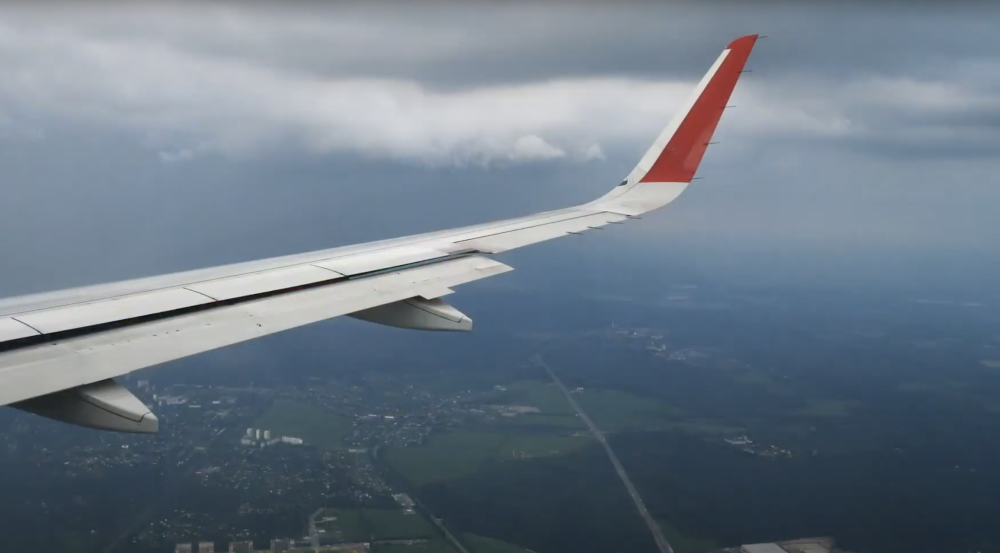 Photo shot from inside of a plane looking out over the plane's wing and green fields below.