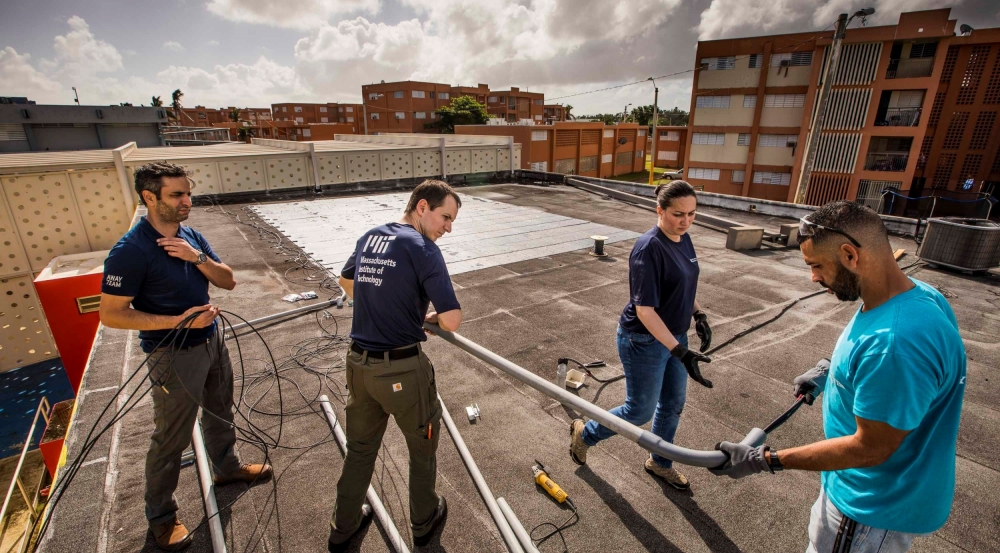 Laboratory staff Erik Limpaecher, center left, and Mabel Ramirez, center right, help run cables down from the solar panels on the roof to a power system inside of the Boys and Girls Club in Las Margaritas, Puerto Rico. Photo: Lorenzo Moscia