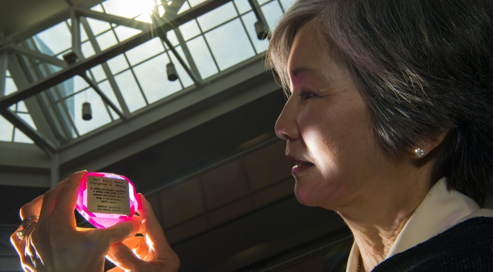 Christine Wang holds her American Association for Crystal Growth Award. The light catches the award, a synthetic ruby inset with a plaque describing the honor.