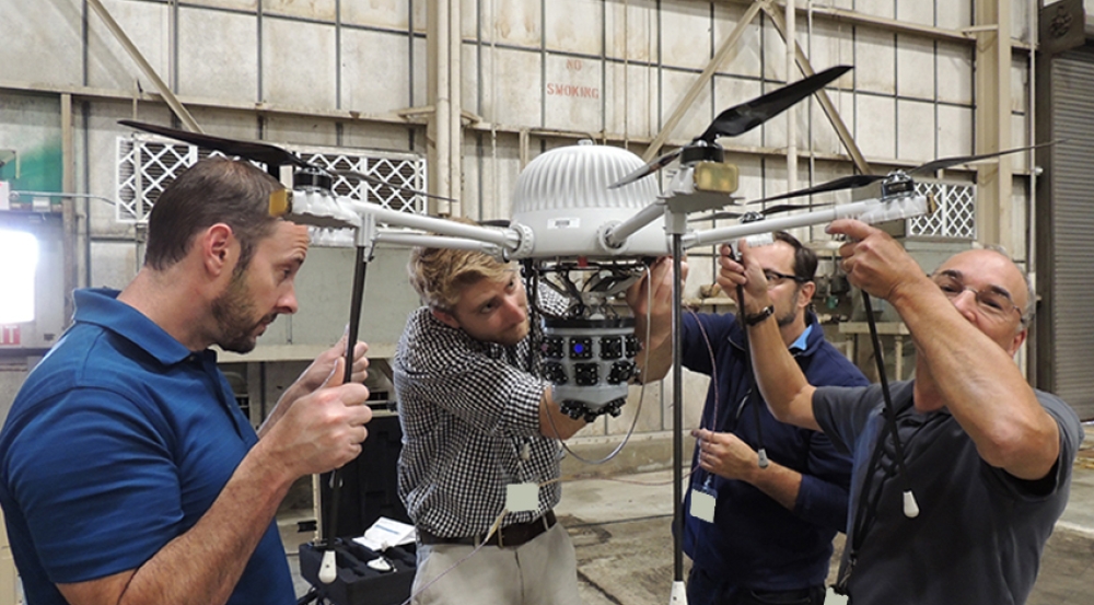 Four people holding up a drone as they work on it.
