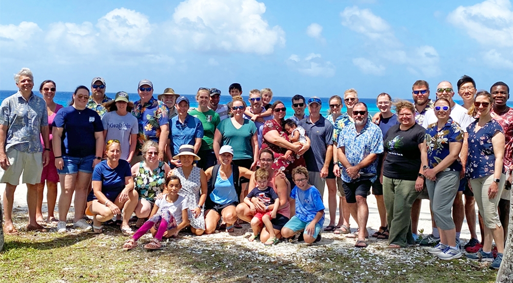 A large group gathers outside near the ocean. 