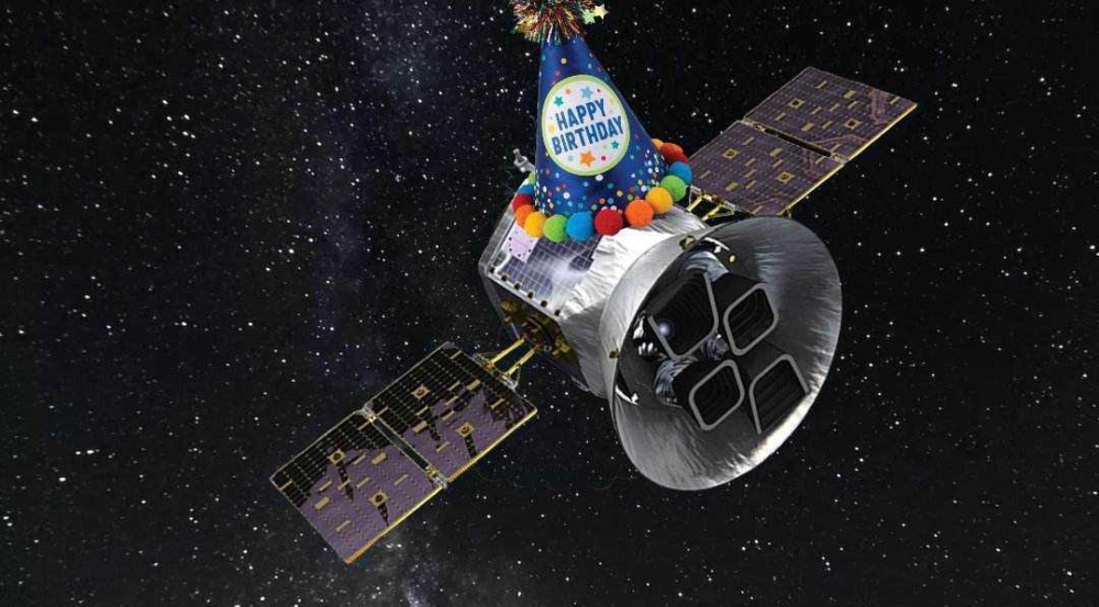 A satellite with a happy birthday hat flies through space.