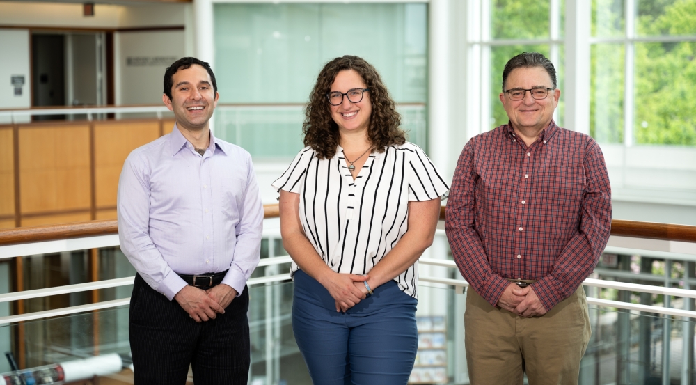 A group photo of three people, smiling for the camera in the Lincoln Laboratory main lobby.