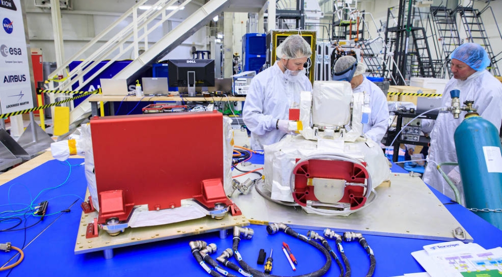 Three people examine an optical communications payload at Kennedy Space Center.