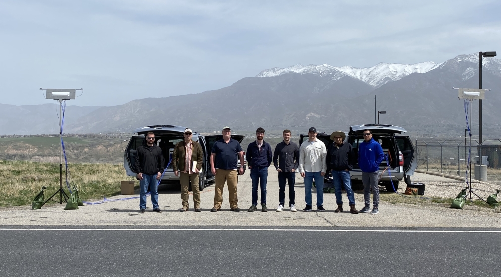 A team of eight stands in front of two sensor-equipped vehicles, with mountains in the backdrop. 