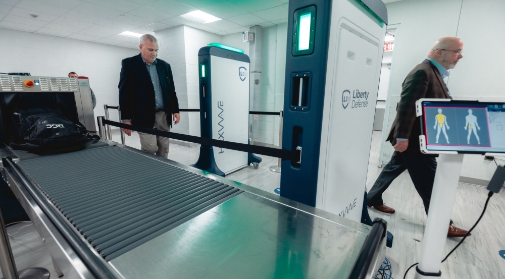 Two individuals walk past a security screening system. 