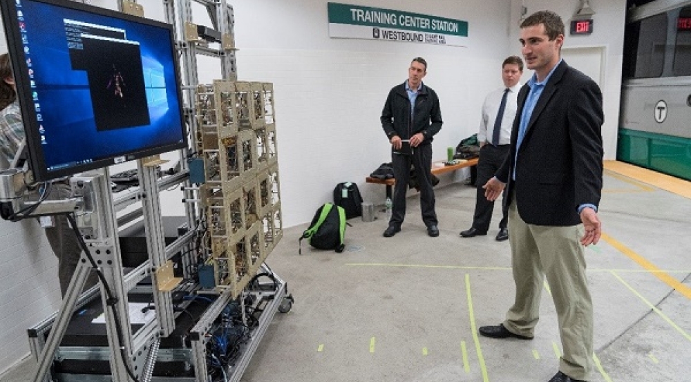 An individual stands in front of an imager as two individuals look on at a subway station platform.
