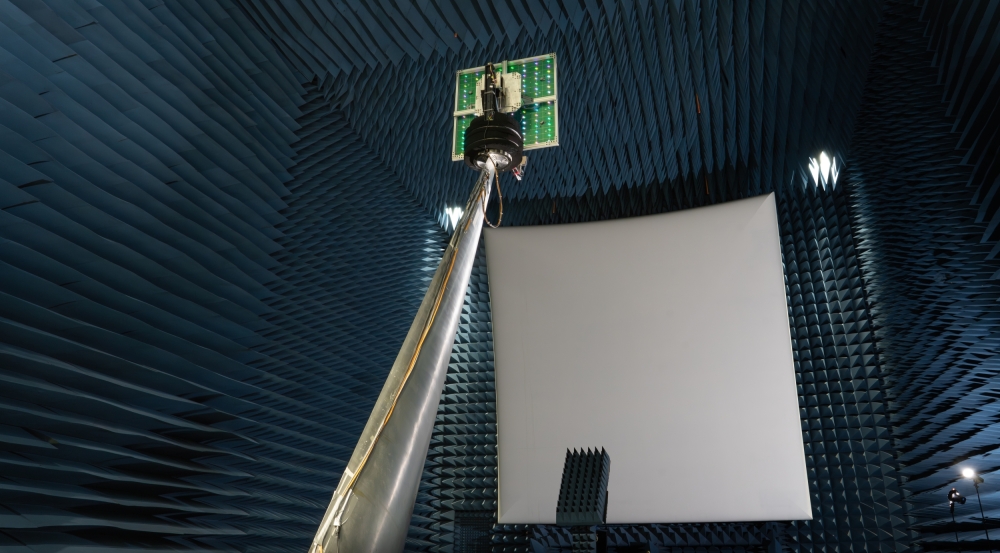 An antenna is held up toward a reflector in an anechoic chamber. 