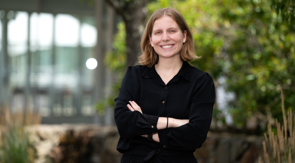 Anna Raymaker smiles for a photo outside of Lincoln Laboratory, with trees and glass facade in the background.
