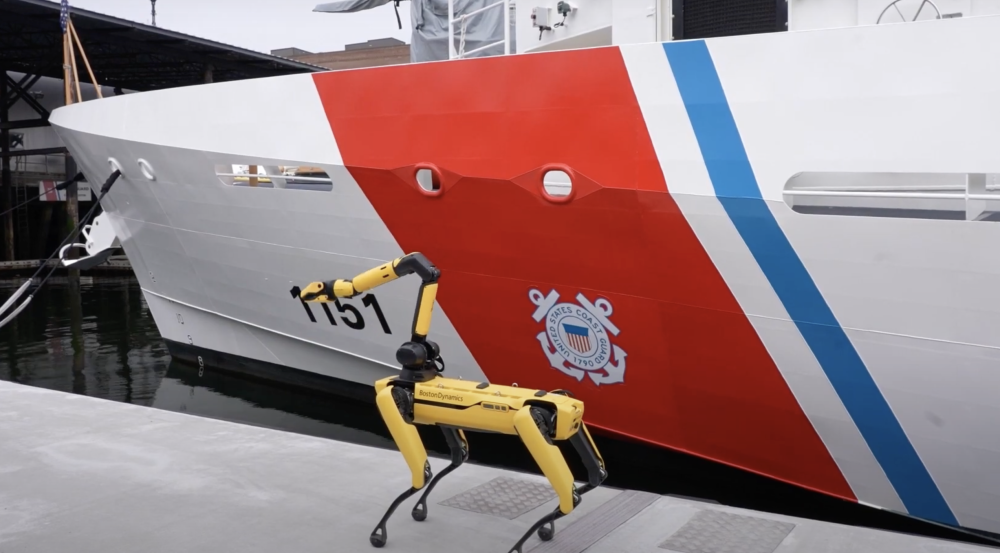 Spot, a yellow robotic quadruped, is on a dock next to a ship. 