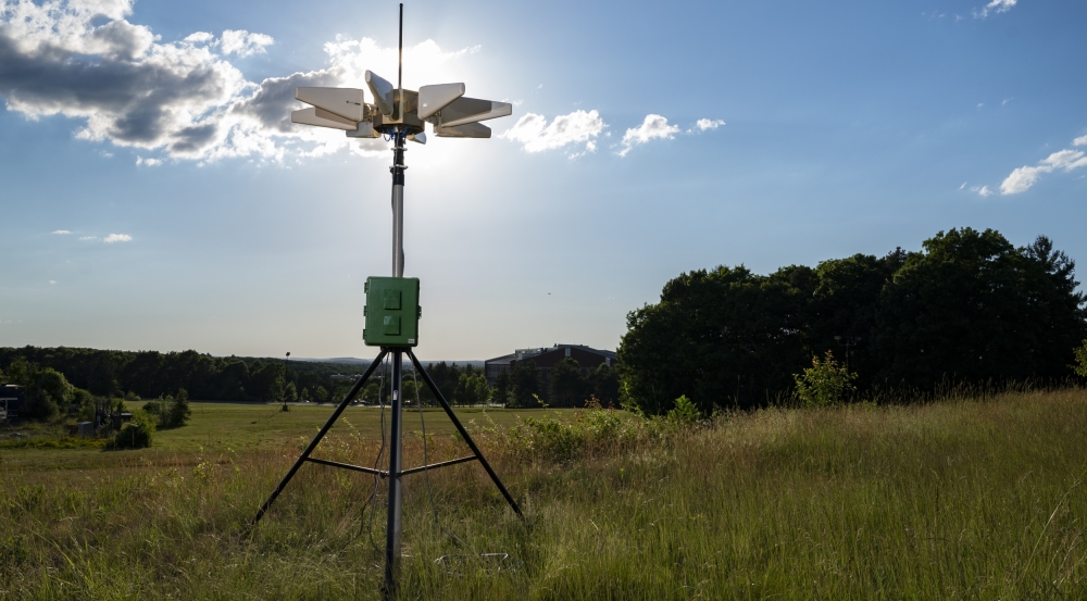 A weather sensor is setup on a tripod in a field.