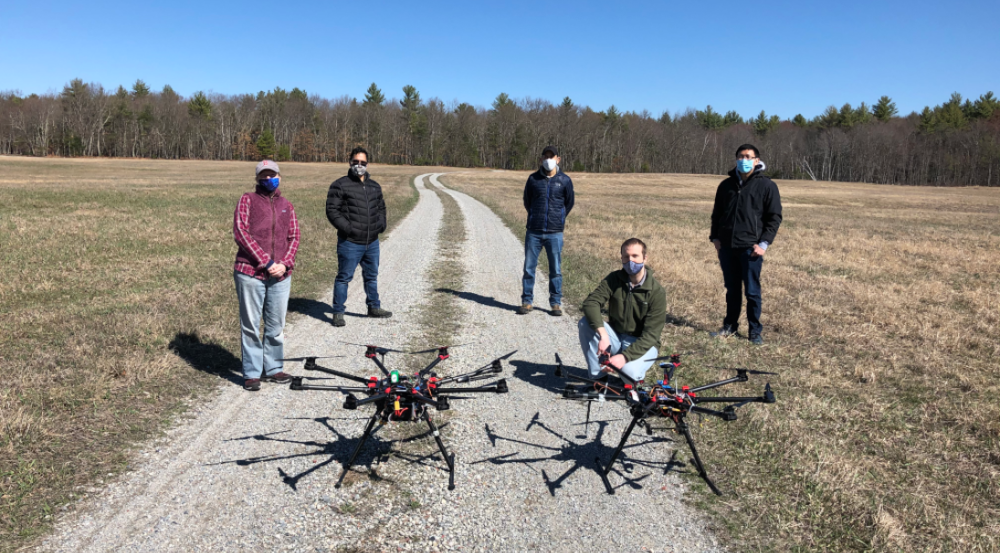 A group of five researchers pose in a field with two UAVs.