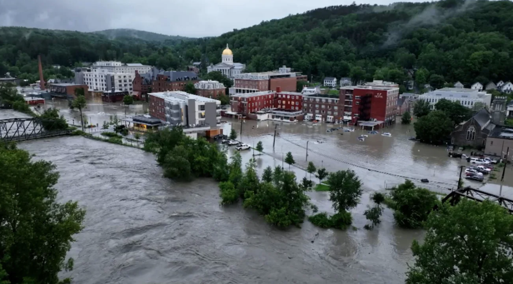 An image showing the flooded streets of Montpelier. Flood water surround brick buildings and roads. 