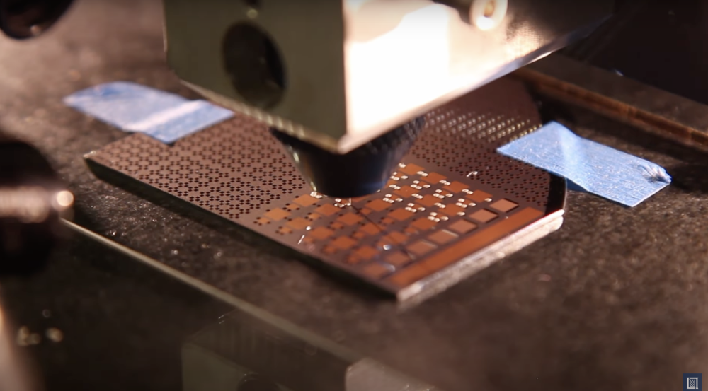a close-up view of a 3D printer head depositing material on a computer chip.