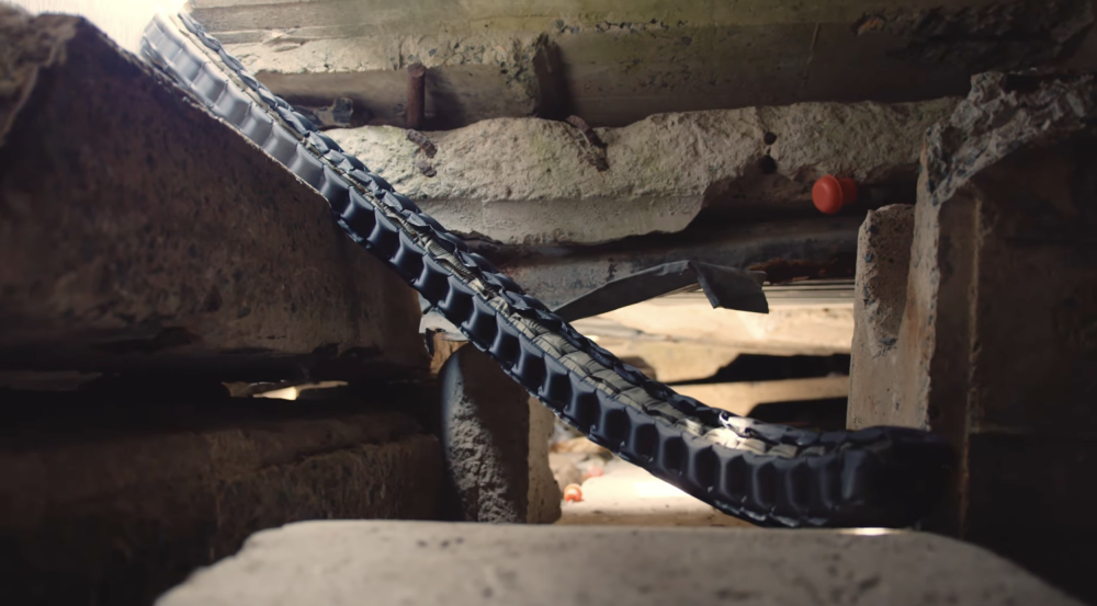 A soft, black fabric tube containing sensors is shown unfurling into a void within broken-down concrete walls. 