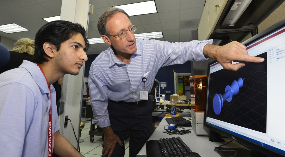 David Scott, manager of TOIL, gives a high school student instructions for using design software to program a 3D printer to build a component.