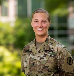 Anna DeVries smiles for a photo outside. Greenery and a building are out of focus in the background. 