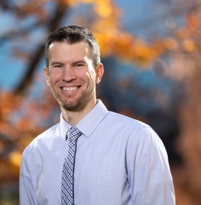 A portrait photograph of Matthew Rebholz, with a blurred fall background.