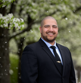 Guillermo Morales smiles for a photo outside a tree with white flowers.