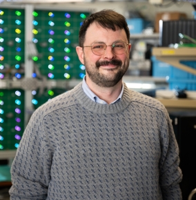 A photograph of Michael Craton standing in front of a reflectarray antenna.