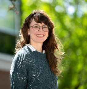 Photo of Emma McDaniel standing outside with a building and green trees in the background. 