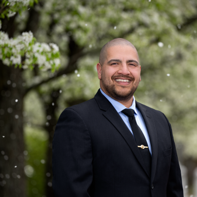 Guillermo Morales smiles for a photo outside a tree with white flowers.