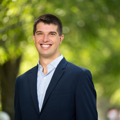 Photo of Nathaniel Hanson smiling with green trees in the background. 
