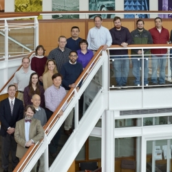 A group of 17 people pose for a photo on a staircase