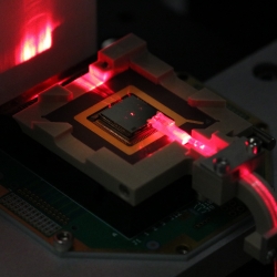 A square electronic chip with a red laser hitting the side of it