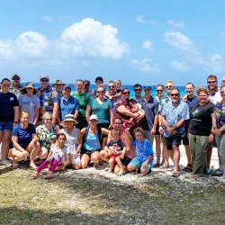 A large group gathers outside near the ocean. 