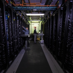 A photo of a hallway between two rows of data center servers. Two researchers are working on the servers.