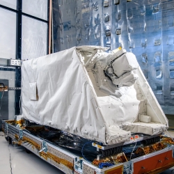 A laser communications terminal approximately the size of a standard refrigerator sits in a cleanroom.