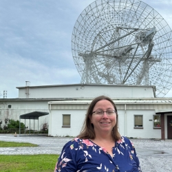 A woman stands in front of a large radar. 