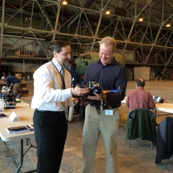 Two individuals hold and look at a drone at an Air Force Base indoor test range.