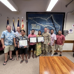 Eight individuals stand together, with three holding certificates.