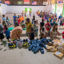 Children and their parents line up in a pavilion to receive shoes during a shoe drive. 