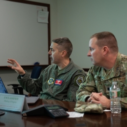 Colonel Joseph Monaco, left, and Lieutenant Colonel Tim Heaton sit at a table discussing a presentation they are being briefed on.