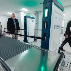 Two individuals walk past a security screening system. 