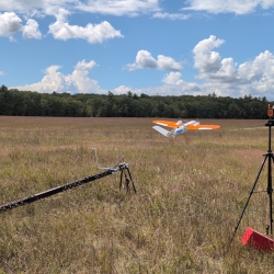 The research team's data collection drone is being launched from a ramp in a field on a clear day. 