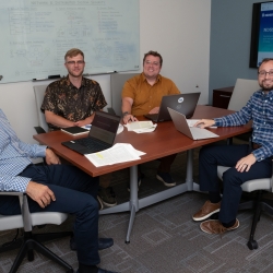 Four researchers sit around a conference table, smiling for a photo. 