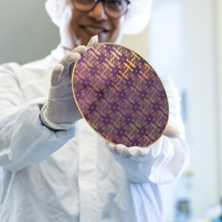 Rabindra Das (wearing microelectronics protective clothing within a fabrication space), holds an 8-inch wafer containing integrated circuits. 
