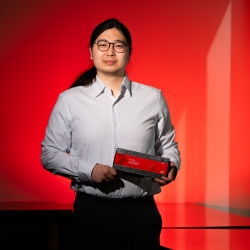 A photo of Jeffery Lim against a red background, holding a hardware platform (rectangle, about 4 by 12 inches). 
