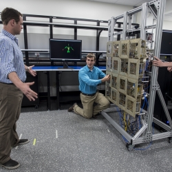 Researchers test the prototype standoff microwave imaging system. The antennas emit radio signals that reflect off the person standing in front of the array; the system processes the reflections to create the image on the monitors in the background.  