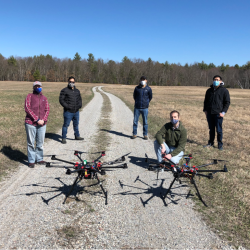 A group of five researchers pose in a field with two UAVs.
